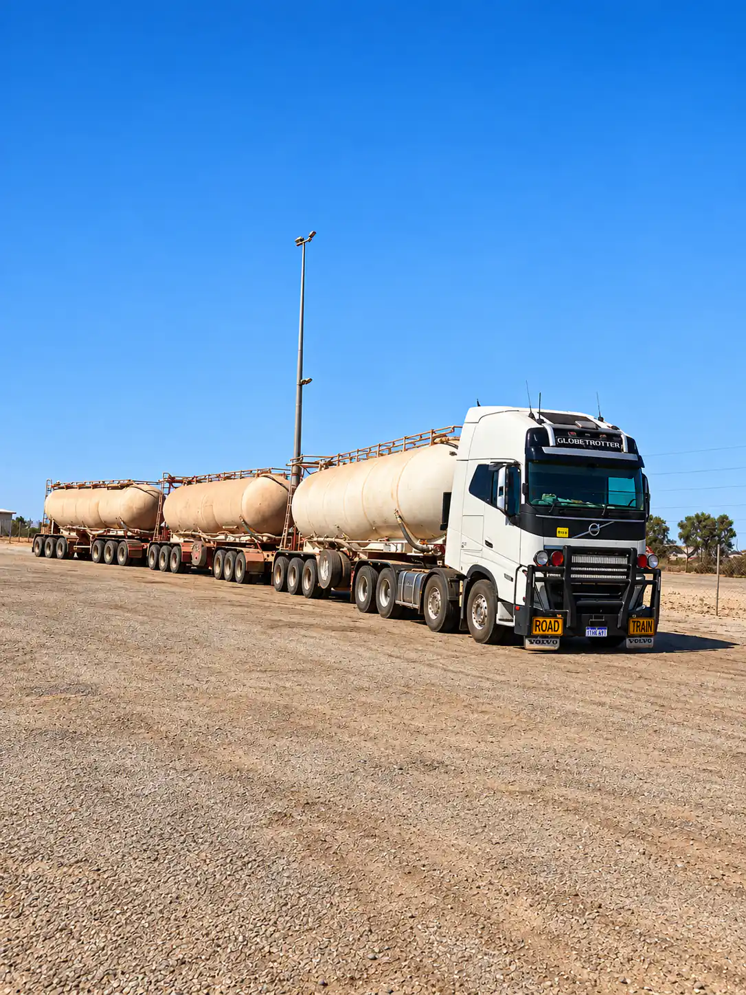 Illustrative white Volvo prime mover with three bulk tanker trailers parked in a transport yard